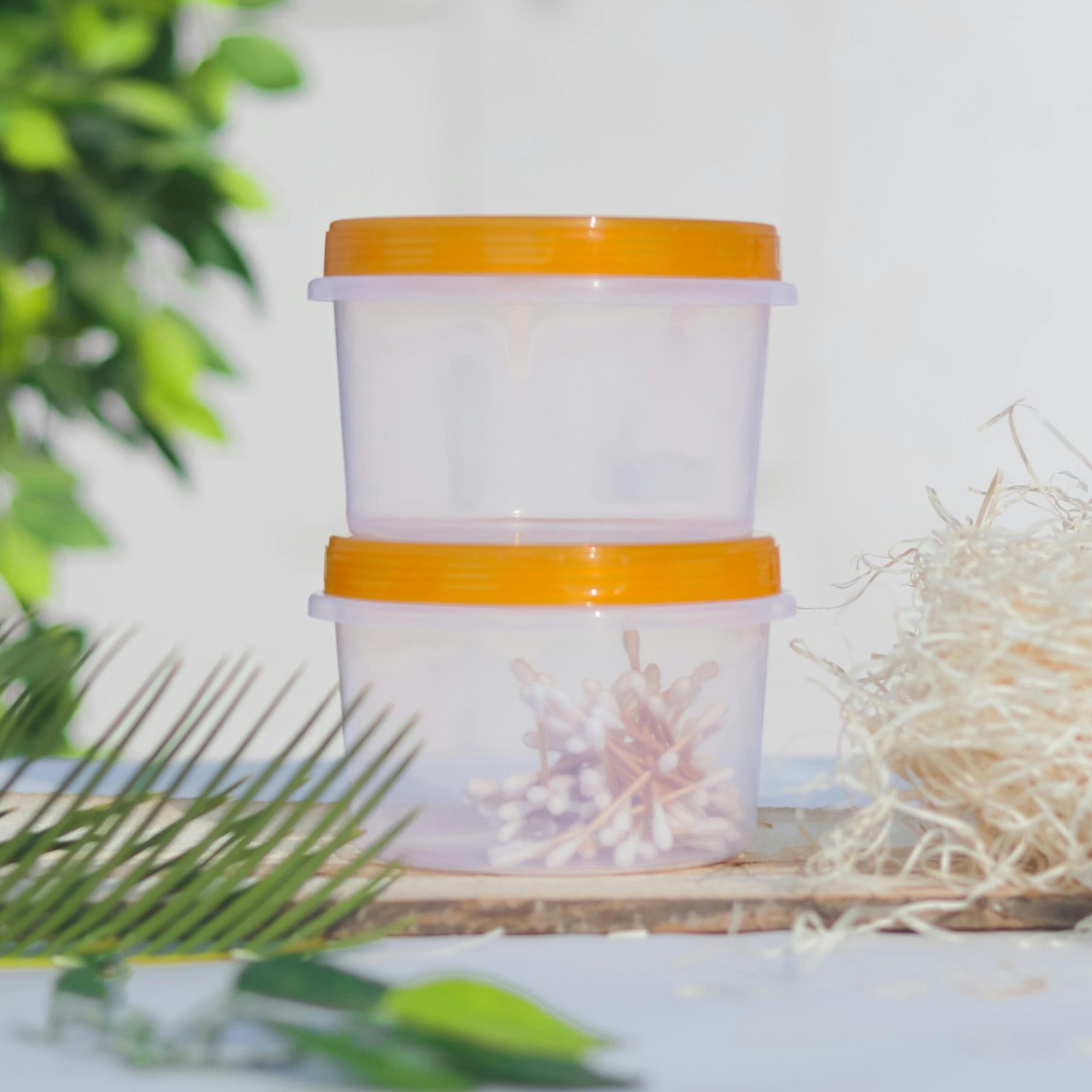 Two stacked plastic containers with cotton buds and orange lids in an outdoor setting.